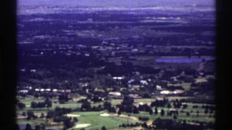 1969 Colorado 8mm frame showing a high view across a golf-course-like foreground toward houses, fields, and hazy hills.