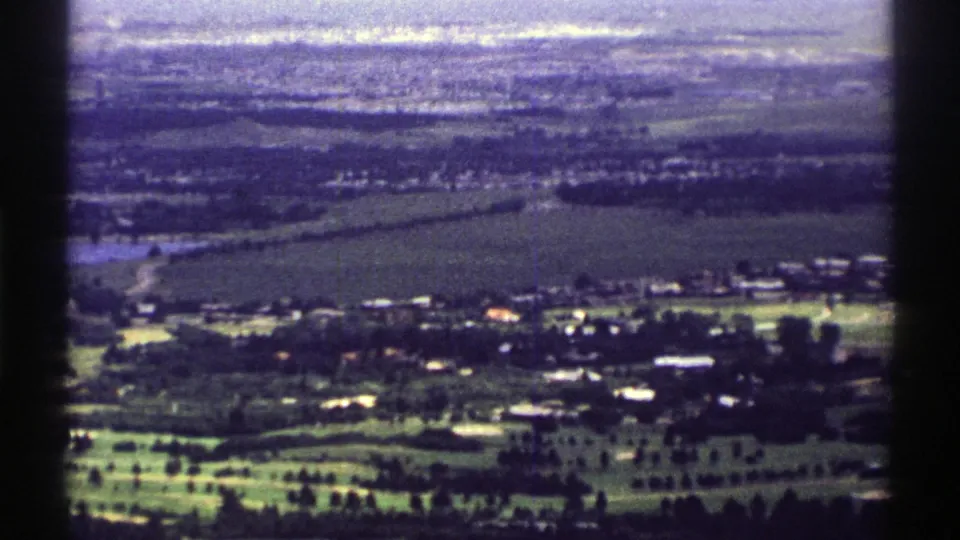 1969 Colorado 8mm frame showing a high view of fields, roads, small structures, and green open land at the town edge.