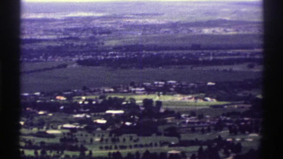 1969 Colorado home-movie frame looking over green fairway-like land, scattered buildings, and a distant rural townscape.