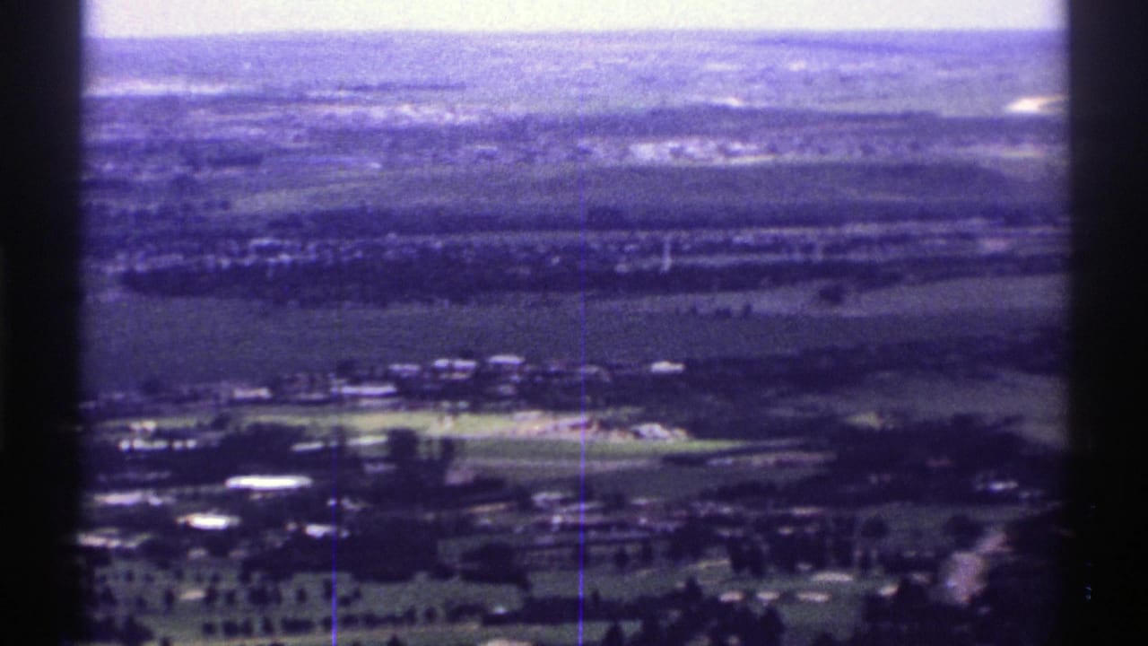 1969 Colorado 8mm aerial frame showing rural fields, small clusters of buildings, roads, and a hazy horizon from an airplane viewpoint.
