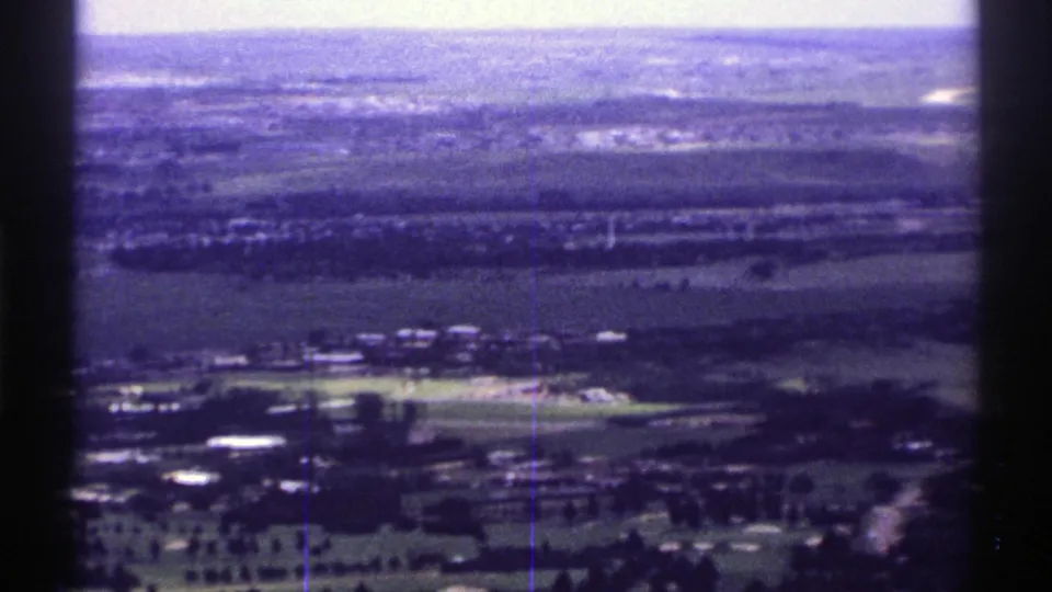 1969 Colorado 8mm aerial frame showing rural fields, small clusters of buildings, roads, and a hazy horizon from an airplane viewpoint.