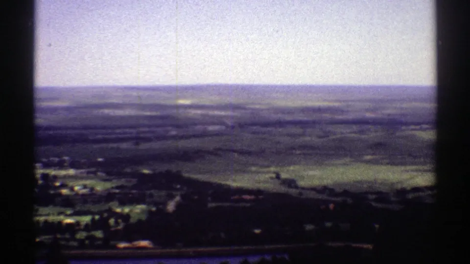 1969 Colorado 8mm aerial frame looking over open rural land, faint road lines, distant hills, and a pale sky near the end of the pan.
