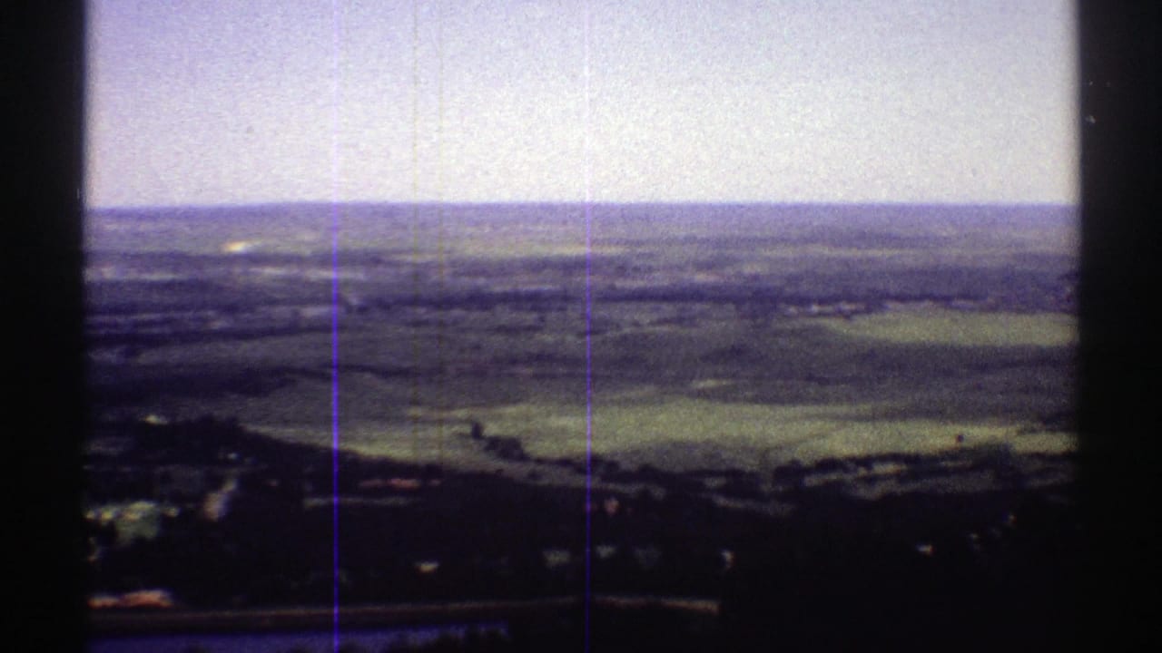 1969 Colorado 8mm view from an elevated overlook across fields, tree-dark slopes, and distant hills under a pale sky.
