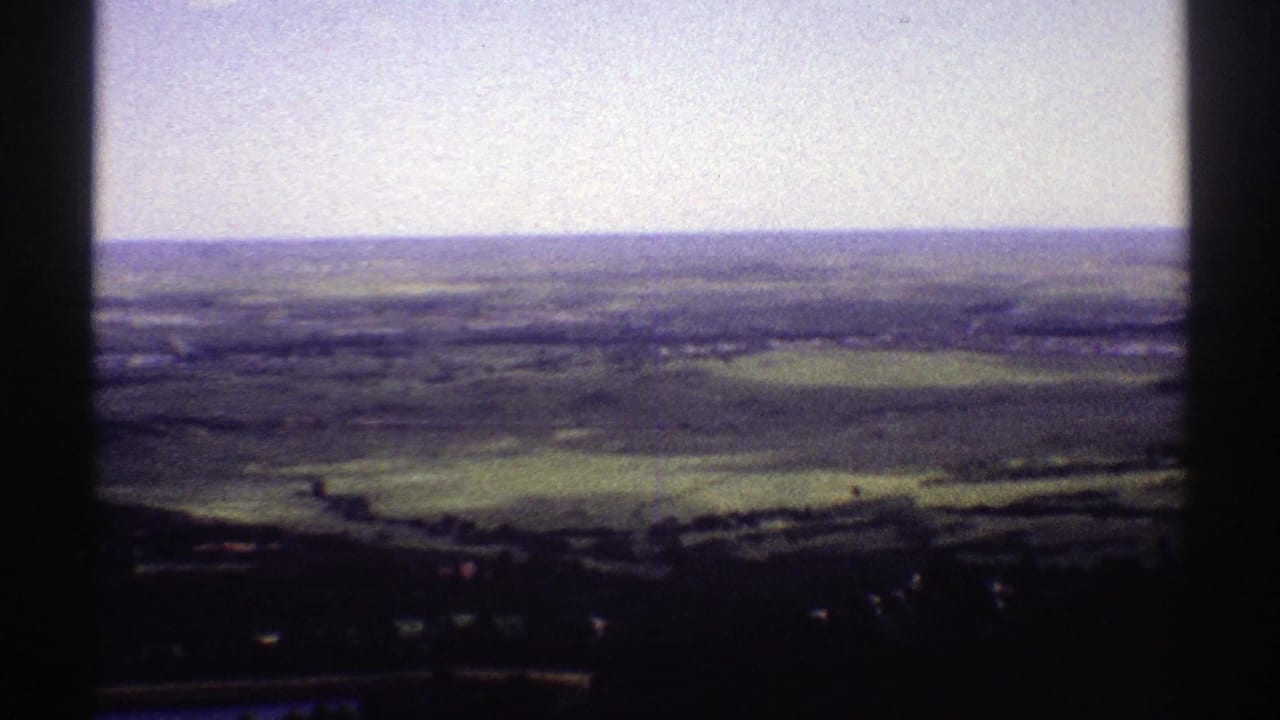 Panoramic countryside view with green fields, distant horizon, and dark vertical frame edge.