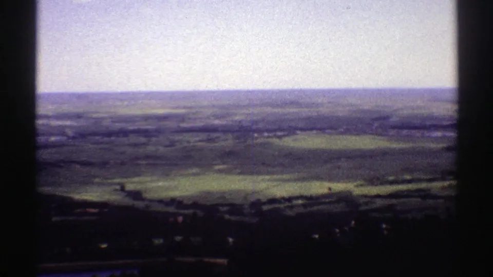 1969 Colorado home-movie frame showing a broad rural valley, patchwork fields, low hills, and prominent film-gate edges.
