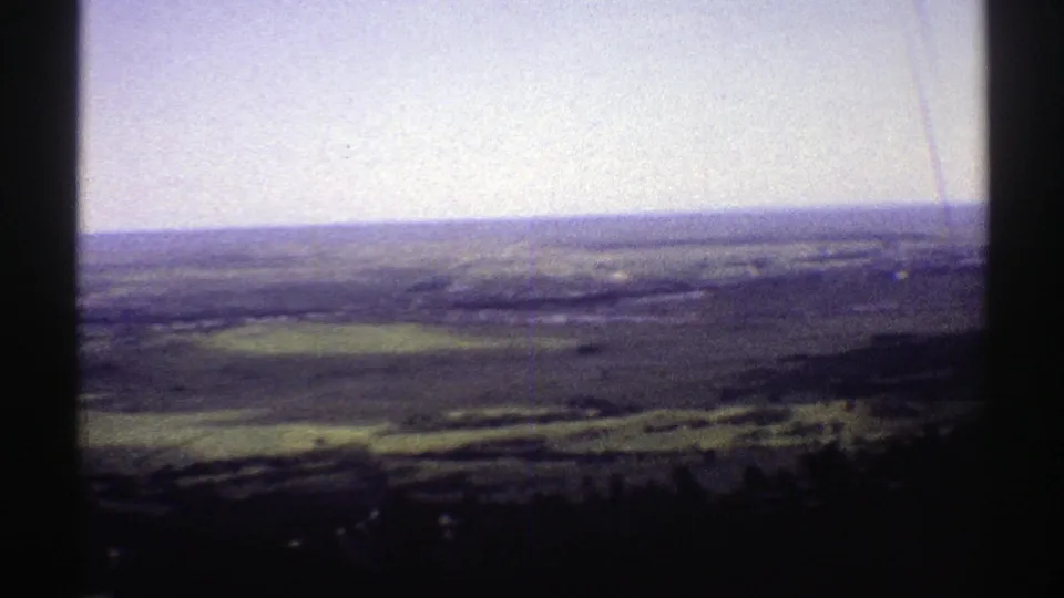 1969 Colorado 8mm frame looking across open countryside from a hill or mountain, with fields and distant terrain softened by film grain.