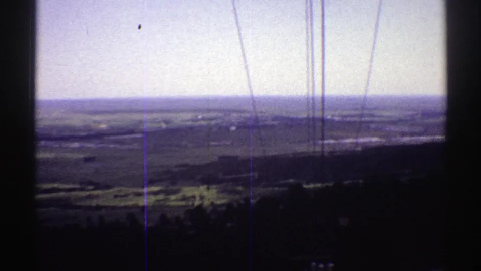 1969 Colorado landscape frame with a shadowed foreground ridge, far fields, pale horizon, and pronounced vertical scratches in the film scan.