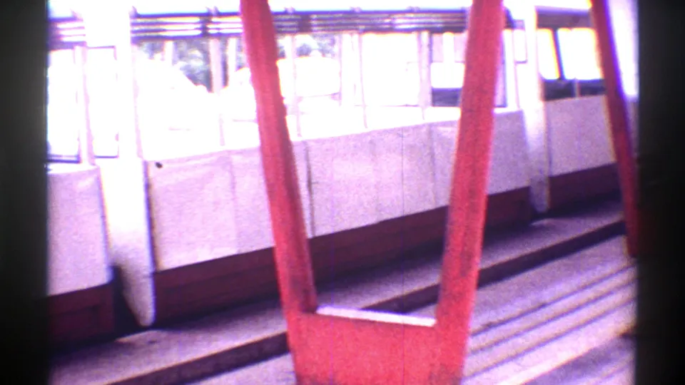 1969 Colorado 8mm frame of red railings, bench seating, and a white zoo tour vehicle or viewing-area structure.