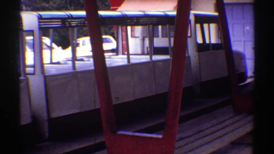 1969 Colorado 8mm view of white-covered wooden benches beneath a roofed shelter, with red framing and a parked car visible outdoors.