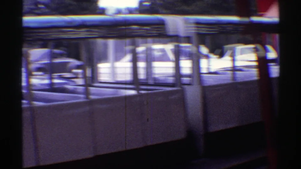 1969 Colorado frame showing the side of an open event shelter with white paneling, dark openings, red framing, and parked cars outside.