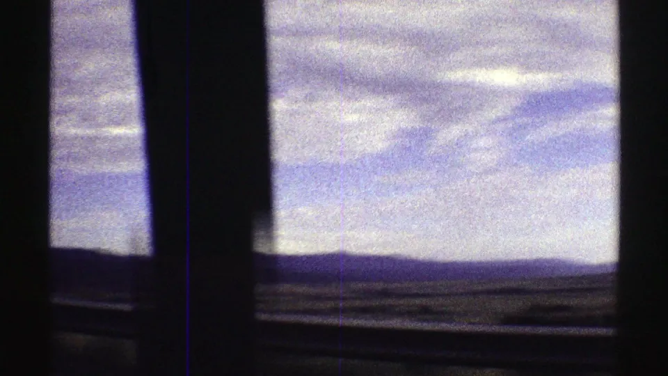 1969 Colorado 8mm frame looking through car-window posts toward low mountains and open terrain beneath a pale cloudy sky.
