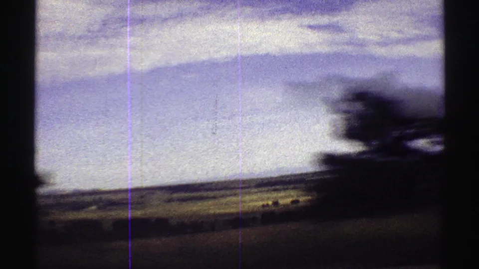 Moving 8mm view across Colorado fields toward distant mountains, with a dark vertical obstruction and soft motion blur in the foreground.
