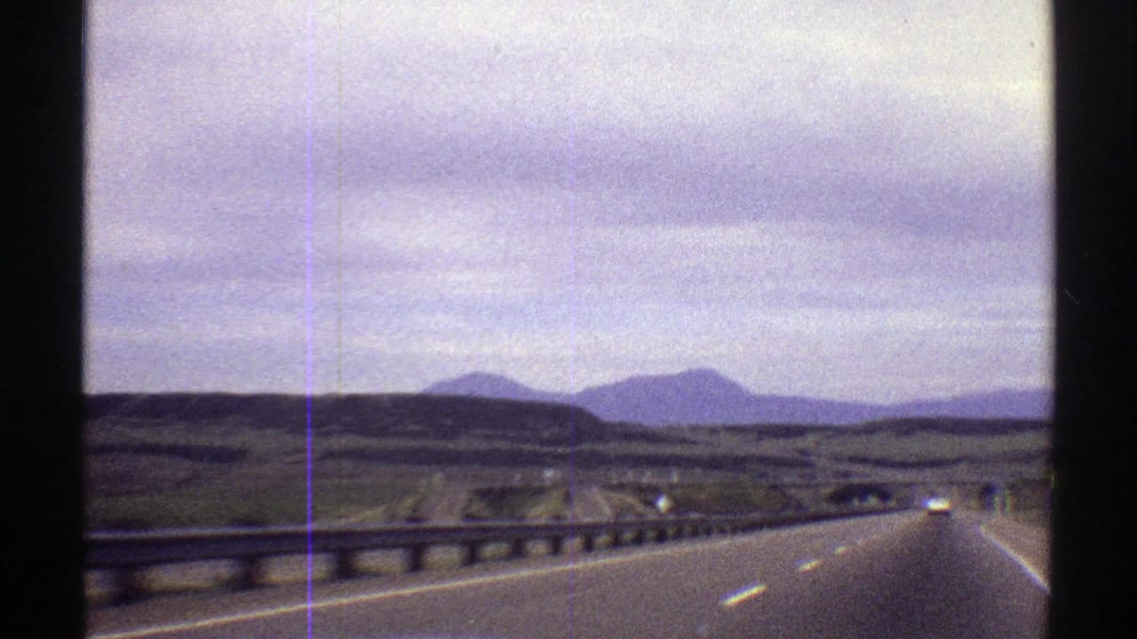 Divided highway running through rolling hills toward distant mountains under an overcast sky.