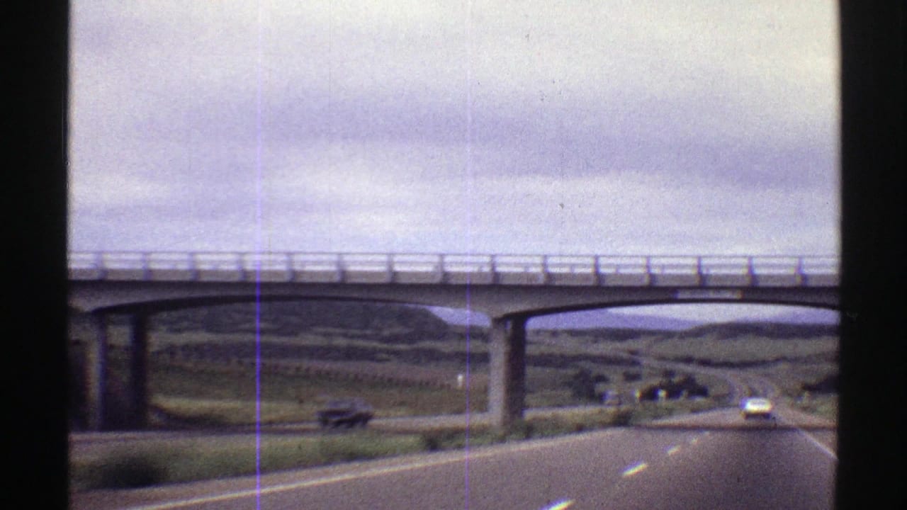 Two-lane highway passing beneath a concrete overpass with cars ahead.