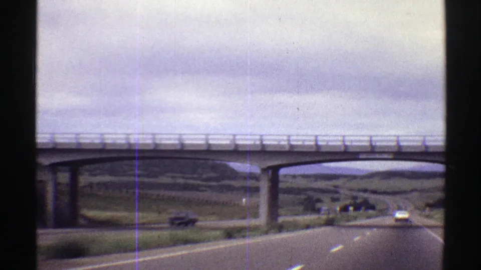 1969 Colorado 8mm view from a moving car approaching a concrete overpass on a rural two-lane highway.
