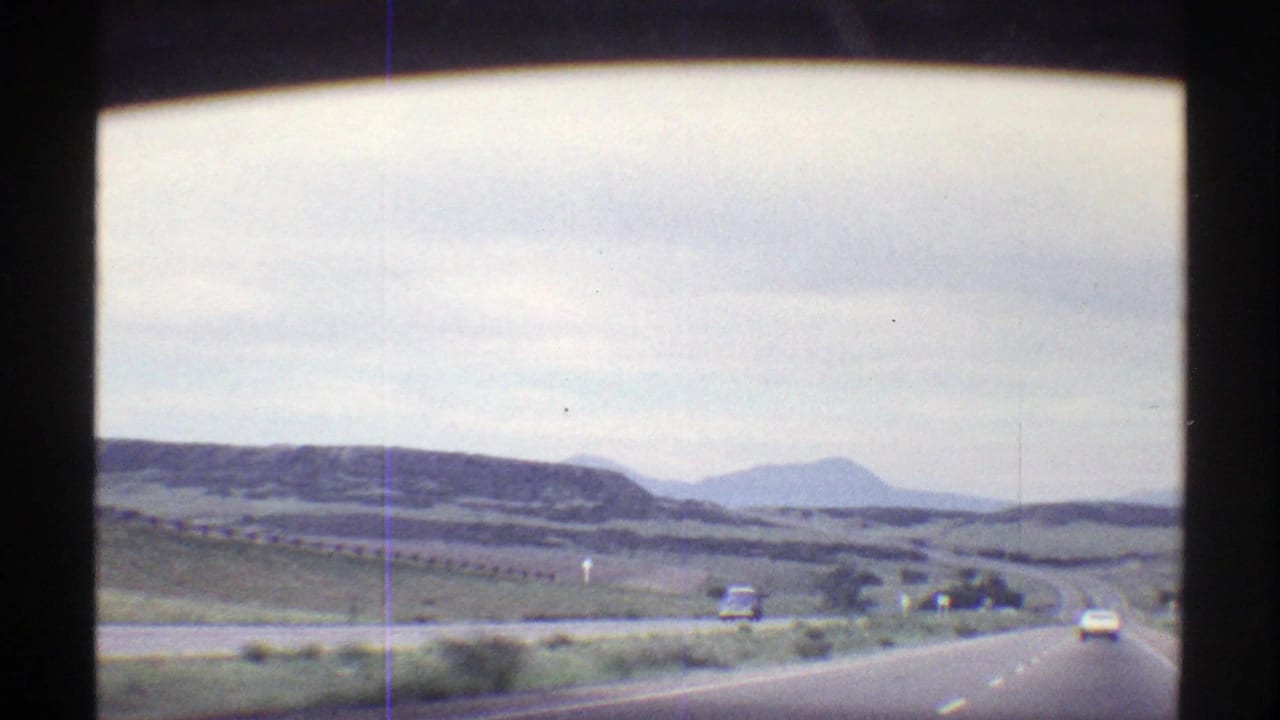 1969 Colorado road-trip view of a two-lane highway with distant cars, low hills, and cloudy sky.