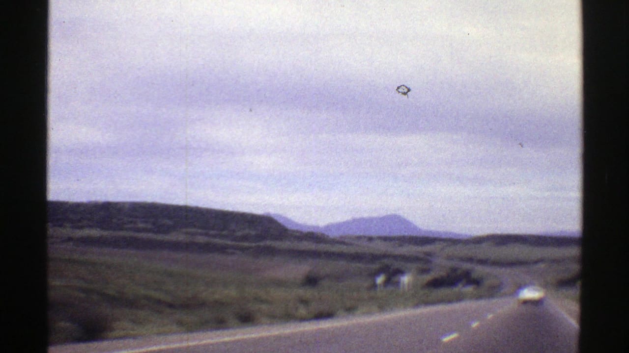 1969 Colorado home-movie view from a car on a rural highway, with open land, distant mountains, and a white car ahead.