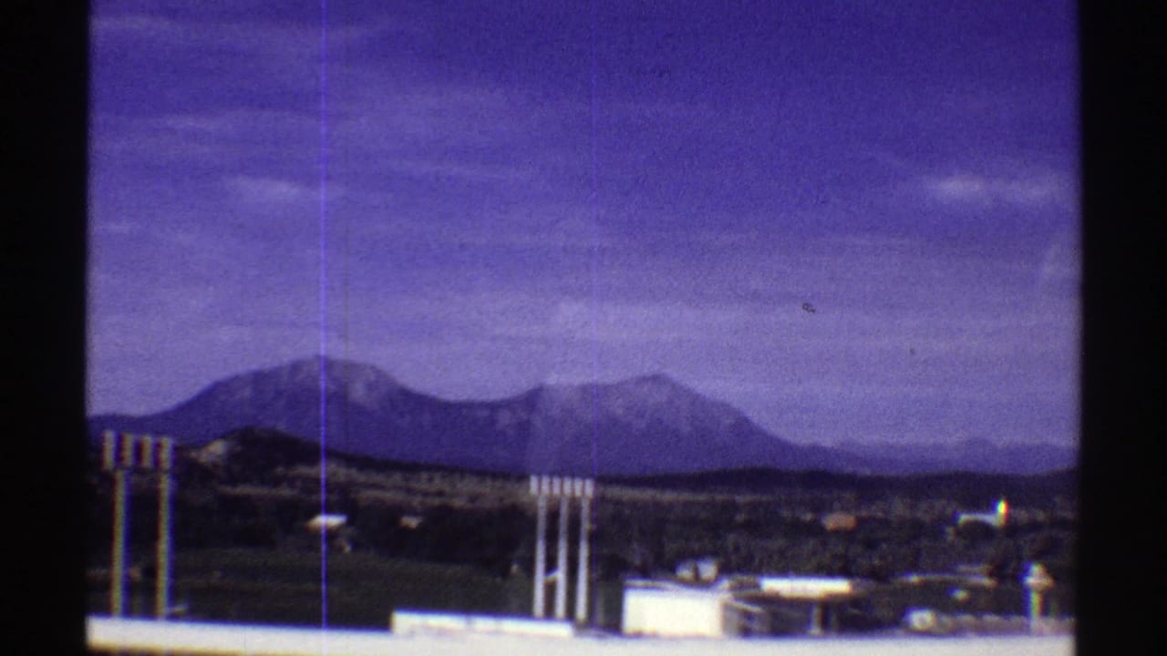 Colorado mountain ridge seen past small roadside buildings and utility poles in purple-shifted 8mm footage.