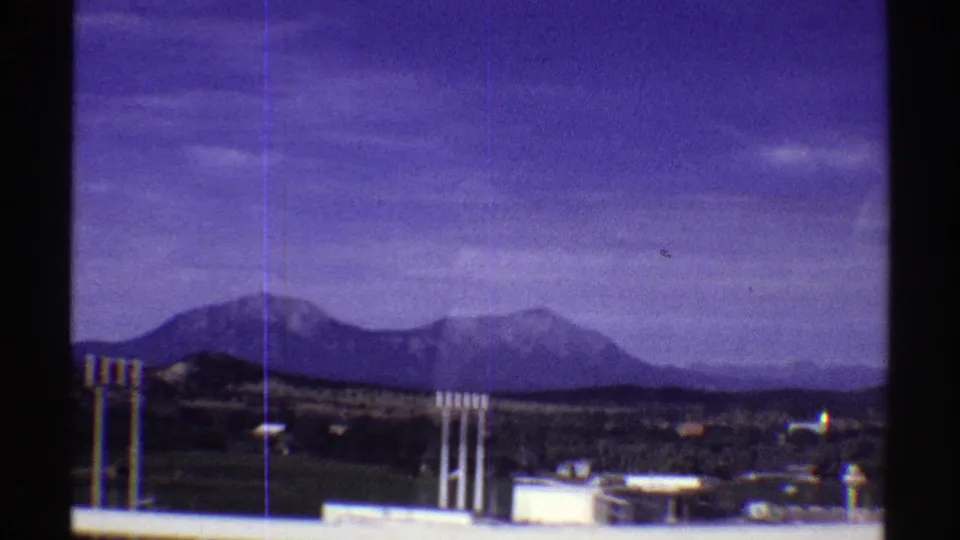 Colorado mountain ridge seen past small roadside buildings and utility poles in purple-shifted 8mm footage.