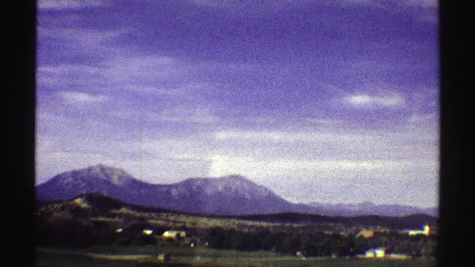 Wide 1969 Colorado home-movie view of mountains beyond open land, scattered buildings, and a clouded sky.