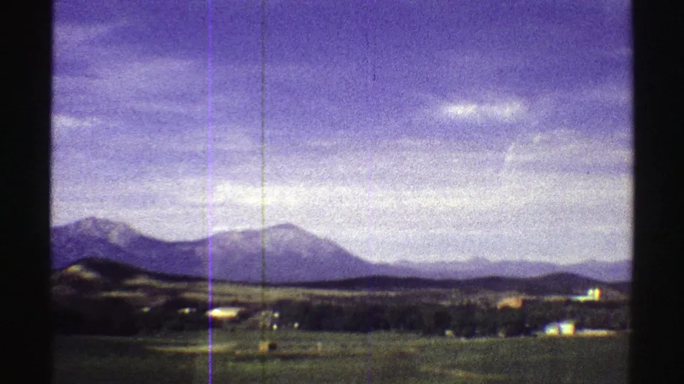 1969 Colorado 8mm frame showing distant peaks, low hills, open ground, and a broad sky with visible film wear.