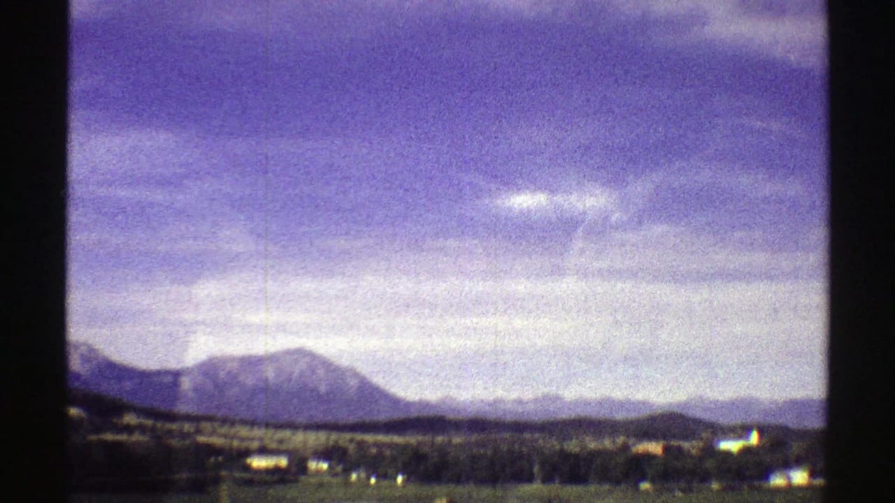 1969 Colorado scenic frame with a mountain ridge, low plains, scattered distant structures, and visible 8mm grain.