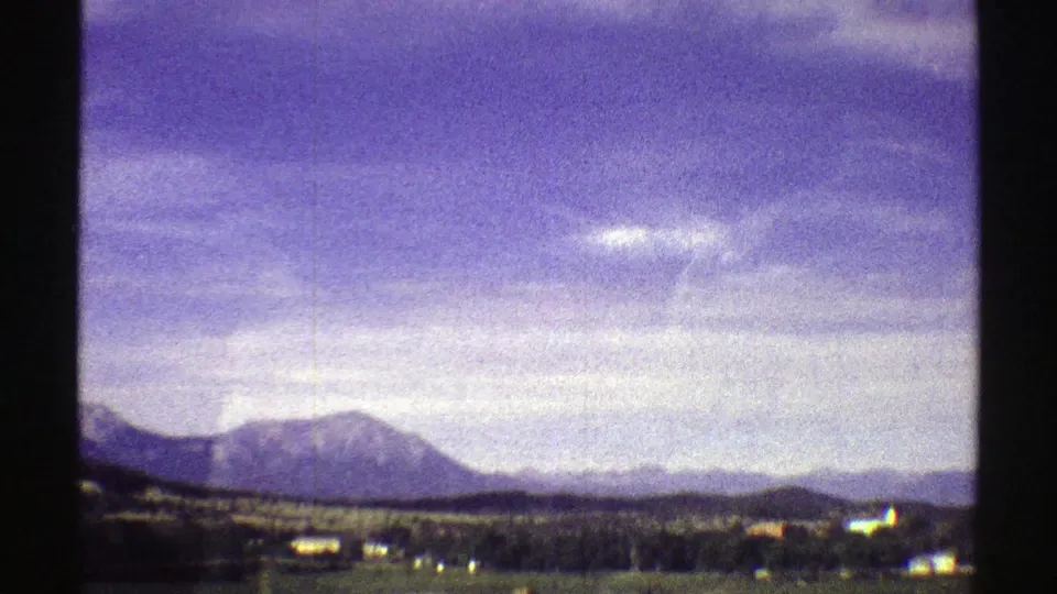 1969 Colorado scenic frame with a mountain ridge, low plains, scattered distant structures, and visible 8mm grain.