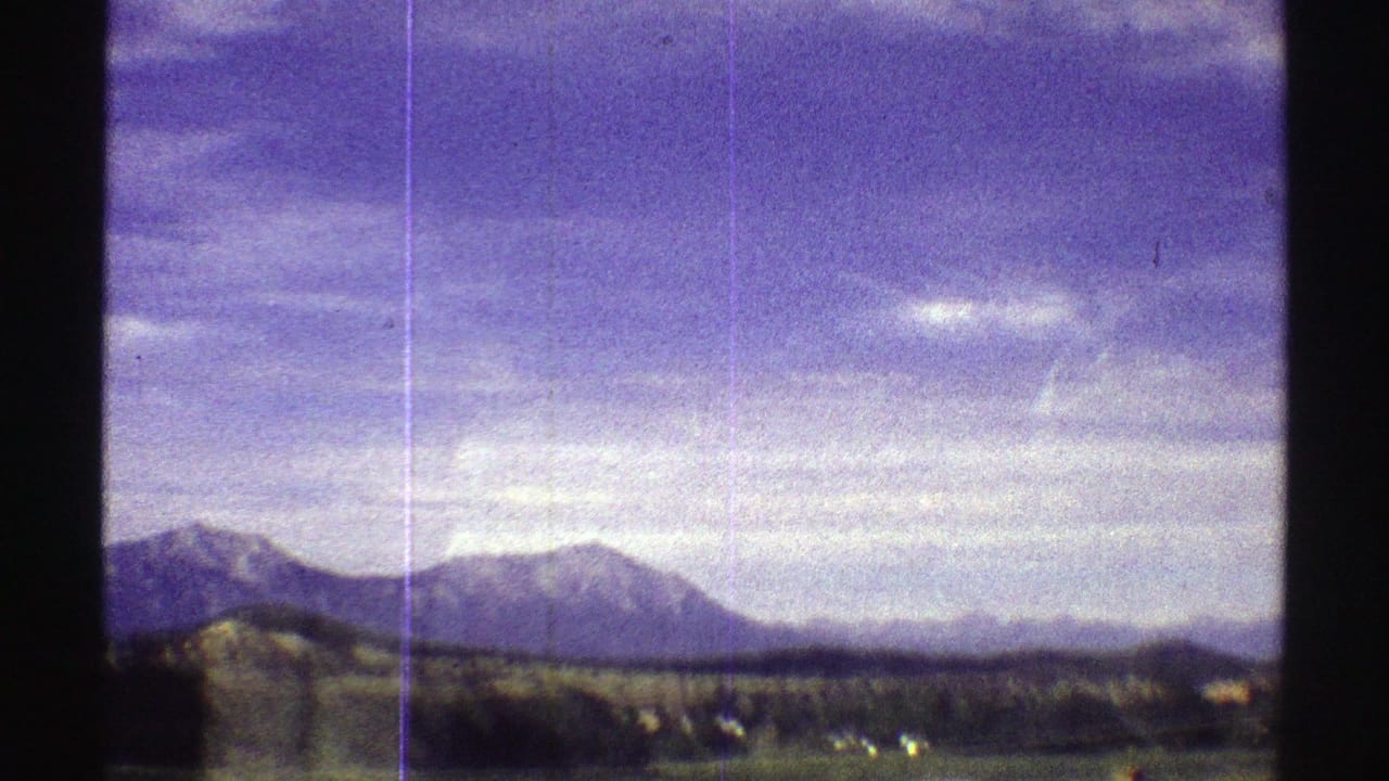 1969 Colorado home-movie frame showing low hills, distant peaks, open ground, and vertical film scratches.
