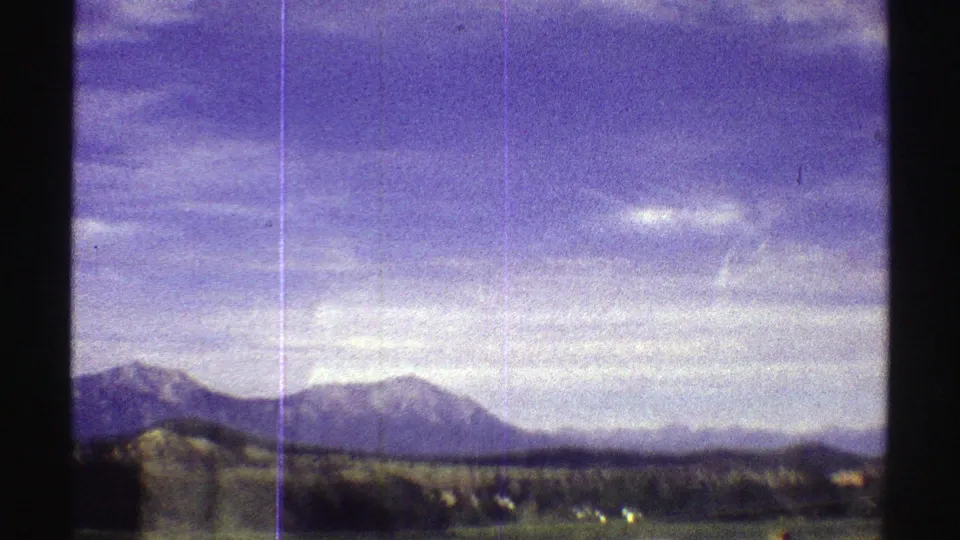 1969 Colorado home-movie frame showing low hills, distant peaks, open ground, and vertical film scratches.