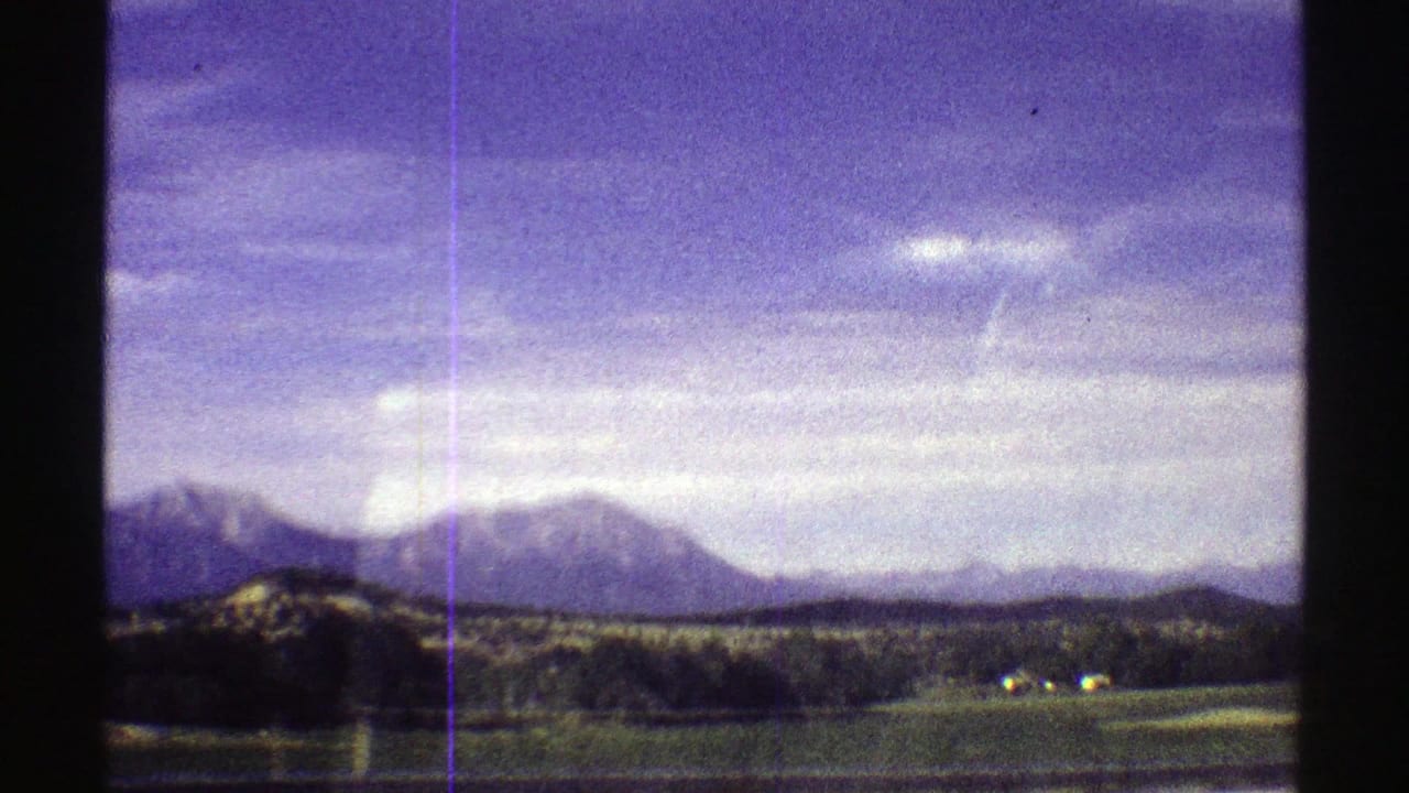 1969 Colorado 8mm frame with distant mountains, open field, tree line, and strong visible film texture.