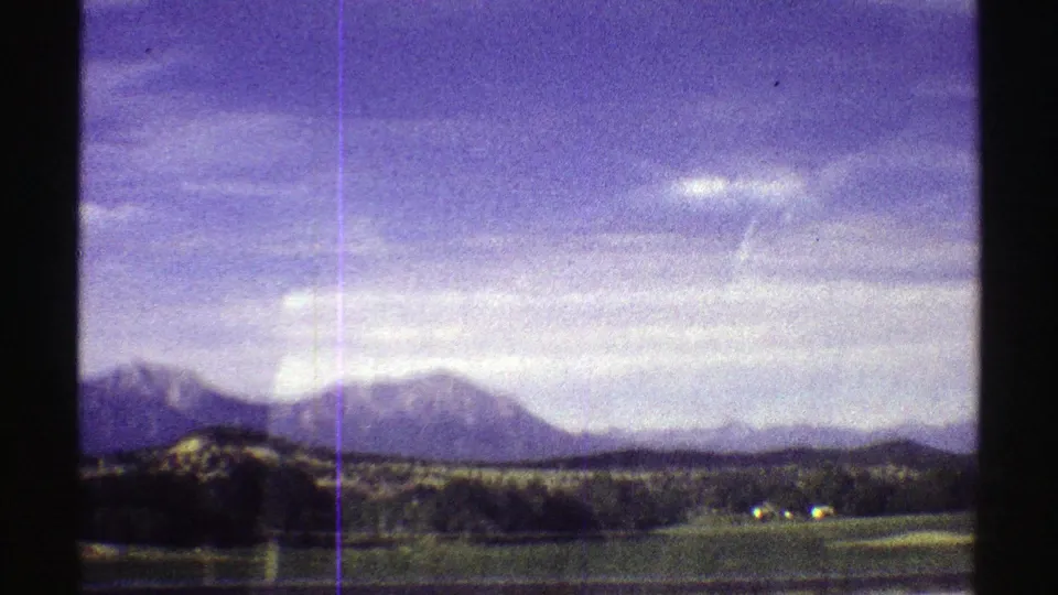 1969 Colorado 8mm frame with distant mountains, open field, tree line, and strong visible film texture.