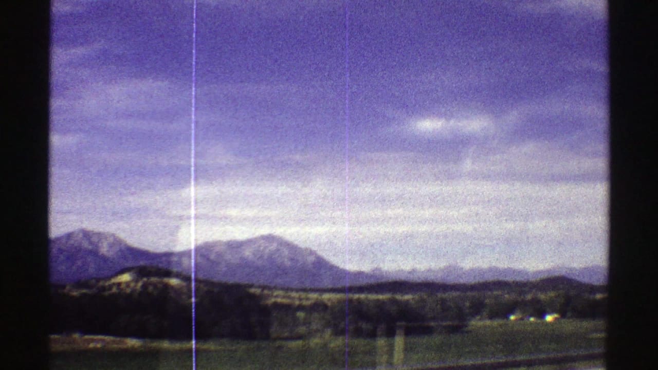 1969 Colorado 8mm frame showing distant mountain peaks, open countryside, and a broad clouded sky with visible film scratches.