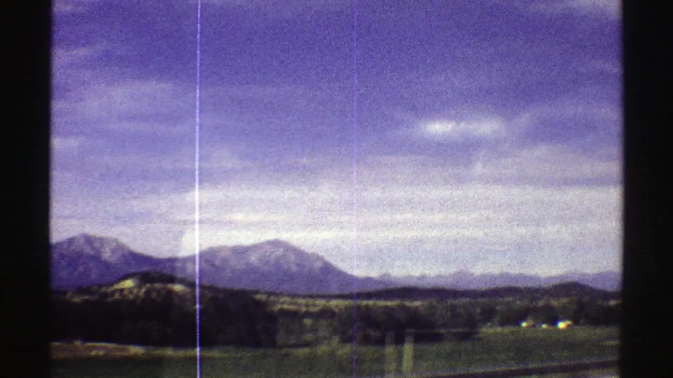 1969 Colorado 8mm frame showing distant mountain peaks, open countryside, and a broad clouded sky with visible film scratches.