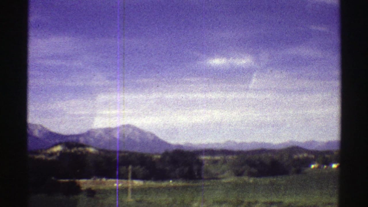 1969 Colorado home-movie view of mountains, rolling land, scattered trees, and a bright sky with blue-purple film color shift.