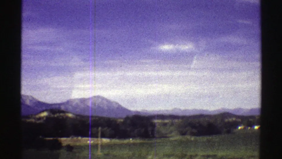 1969 Colorado home-movie view of mountains, rolling land, scattered trees, and a bright sky with blue-purple film color shift.