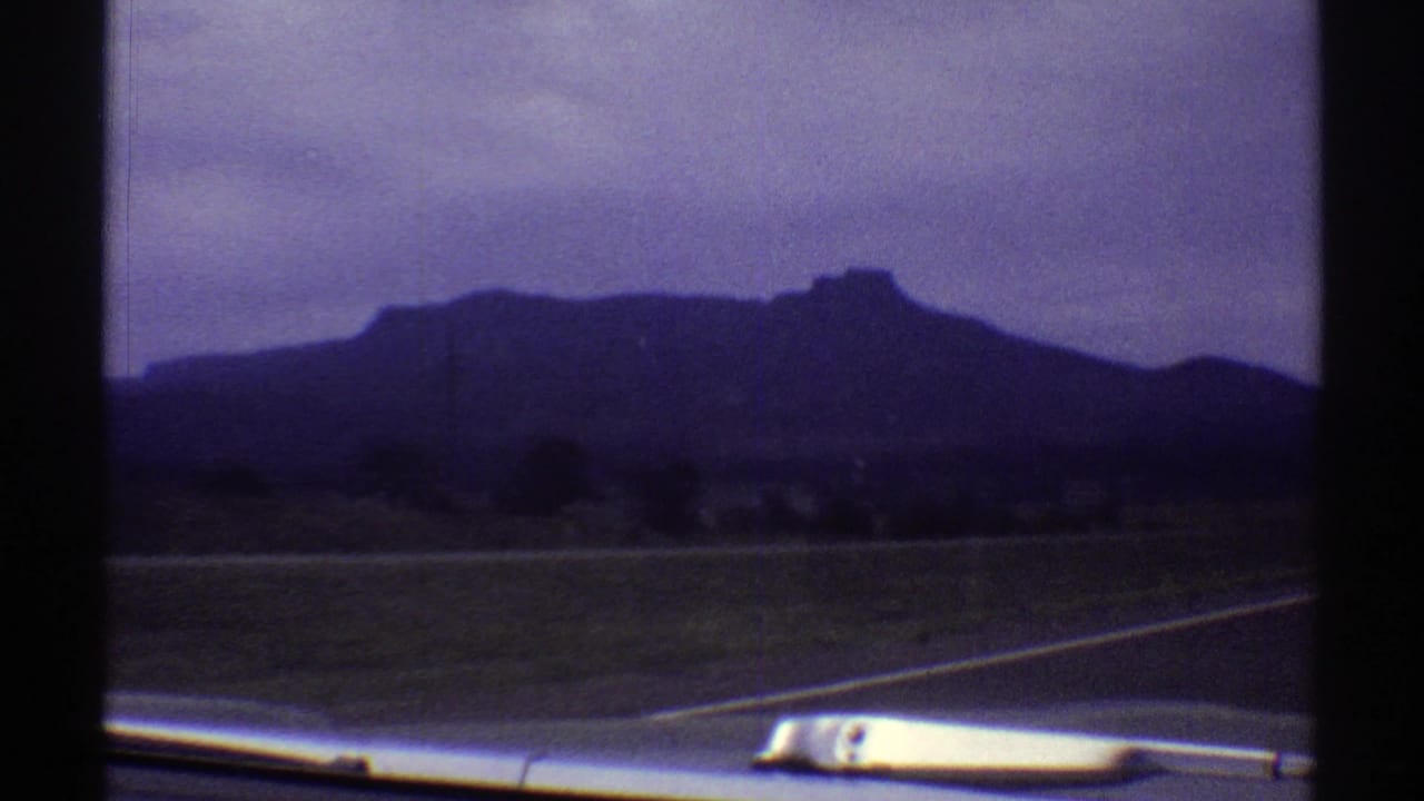 1969 Colorado road-trip frame with a mesa-like ridge, roadside foreground, and part of the vehicle dashboard visible below.