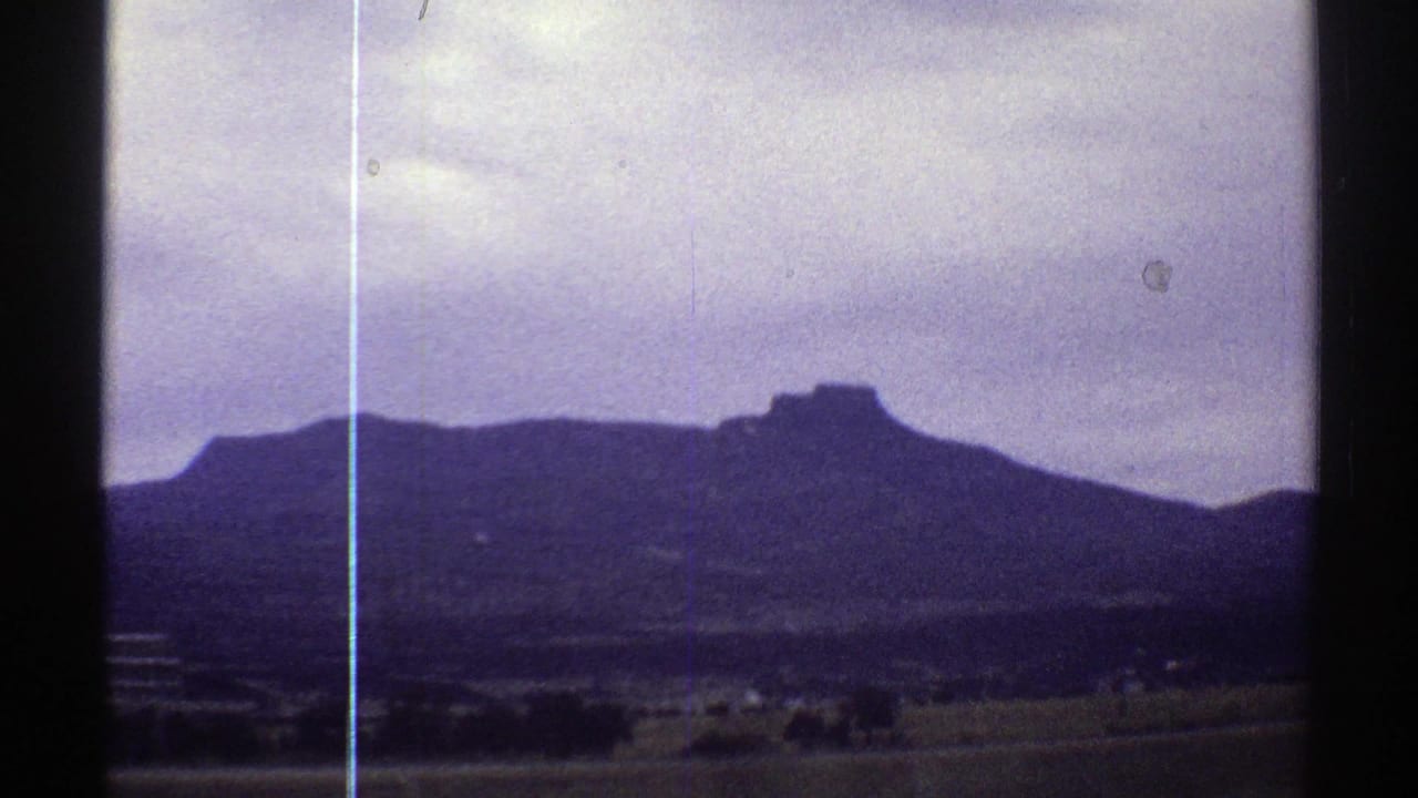 Mountain ridge and open rural land seen through a dark film-frame edge.
