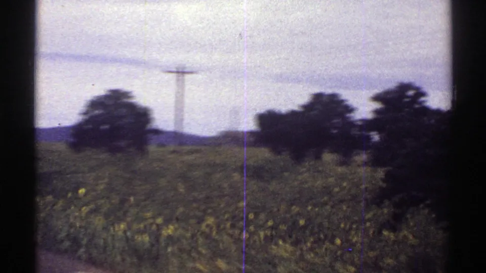 1969 Colorado 8mm roadside frame with blurred vegetation, utility poles, low hills, and dark window framing from a moving car.