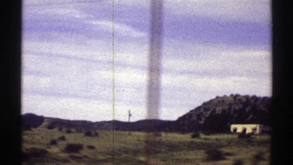 1969 Colorado countryside frame showing open grassland, low hills, scattered trees, and a small distant house under cloudy sky.