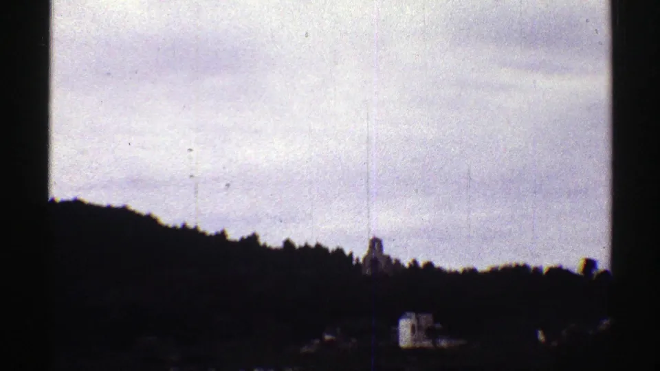 1969 Colorado 8mm frame showing a silhouetted ridge, pale clouded sky, and a small town structure with a steeple-like profile.