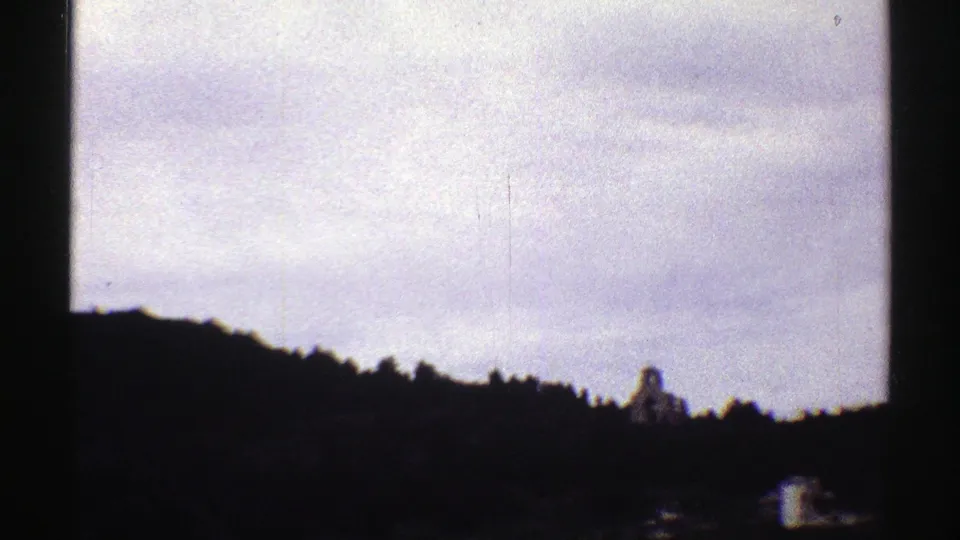 Faded 1969 Colorado road-trip frame with hillside horizon, distant town buildings, and a steeple-like structure at the edge of view.