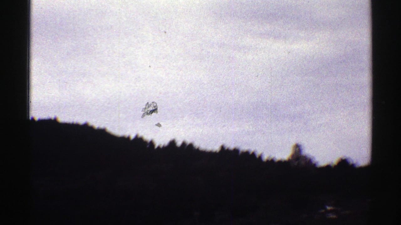1969 Colorado 8mm frame showing pale overcast sky over a dark wooded ridge, with heavy shadow and visible film wear.