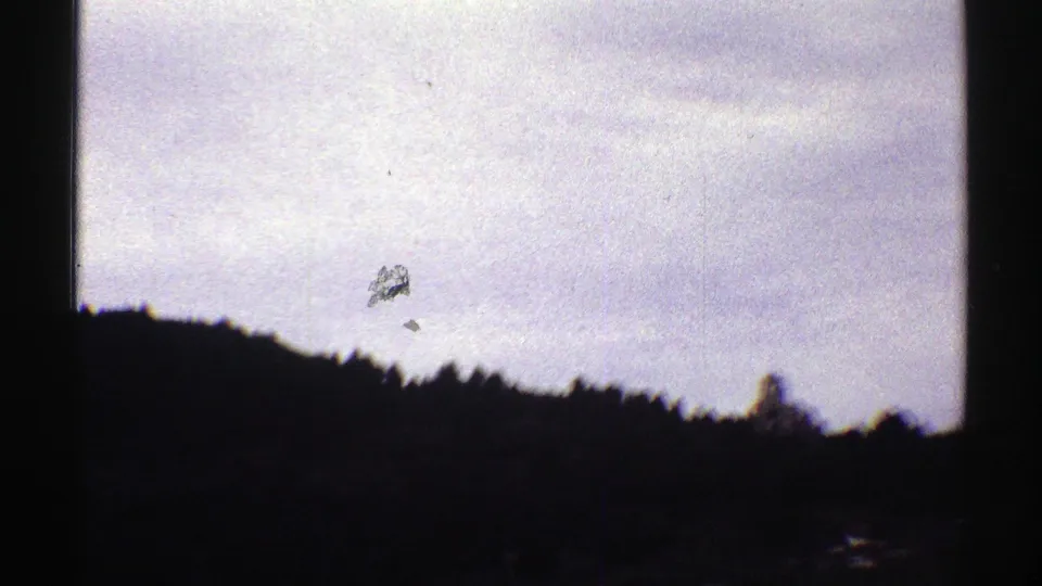 1969 Colorado 8mm frame showing pale overcast sky over a dark wooded ridge, with heavy shadow and visible film wear.