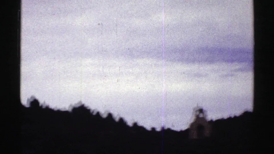 1969 Colorado 8mm view of a bright cloud field, silhouetted hillside, and a small distant structure near the lower edge.