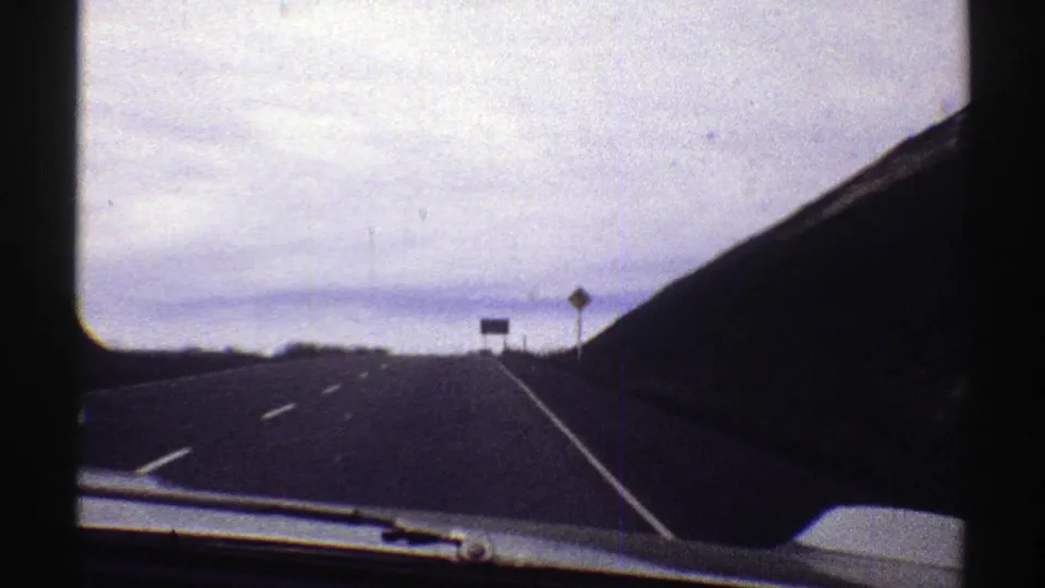 1969 Colorado road view from a moving car, showing an open highway, roadside signs, and a dark mountain slope.