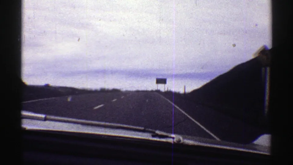 1969 Colorado driving view through a car windshield, with highway lines, signs, hillsides, and muted 8mm color.