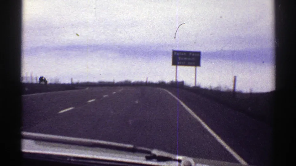 1969 home-movie frame from a car nearing a green sign that reads Raton Pass Summit next exit.