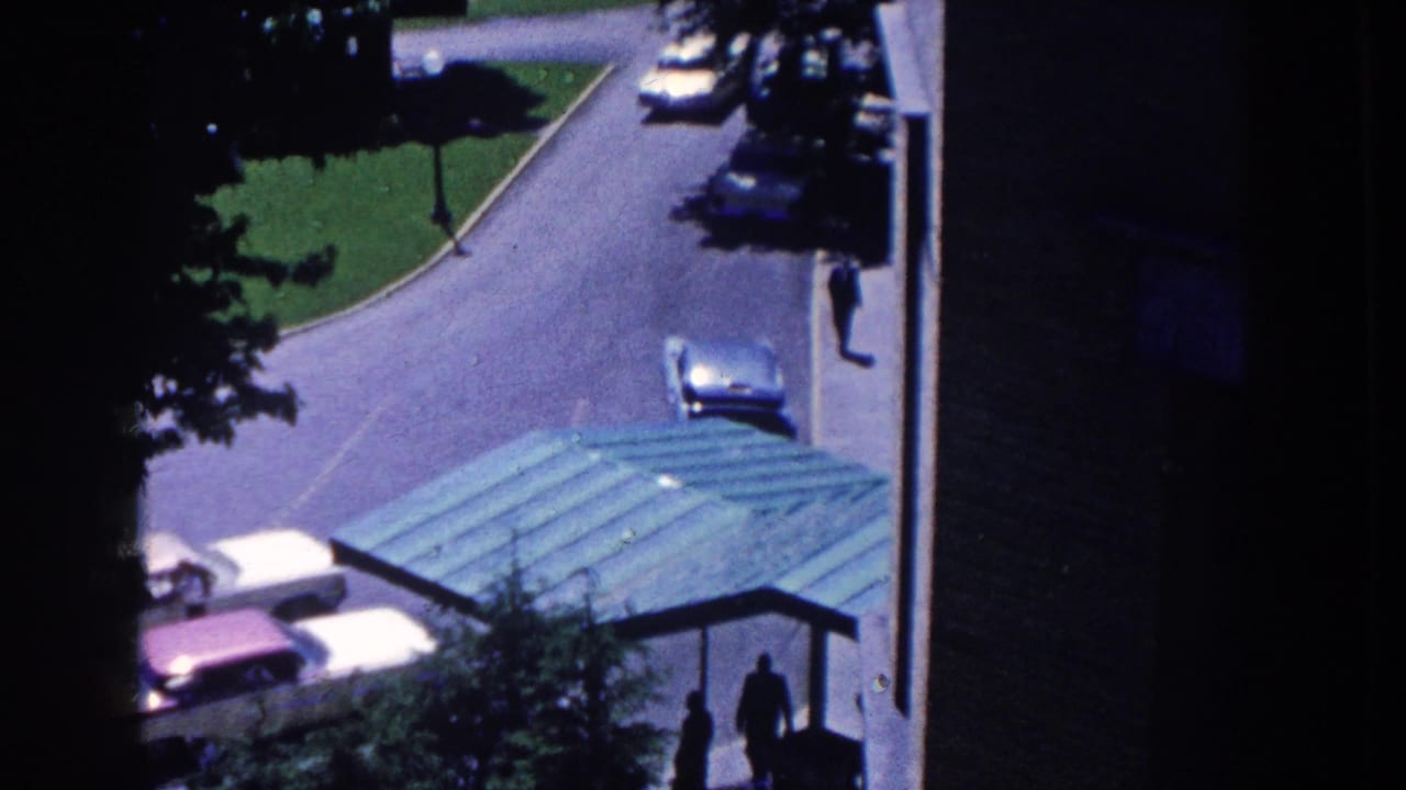 1958 French Lick hotel driveway seen from above, with late-1950s cars, a green porte-cochere roof, trees, and silhouetted pedestrians.