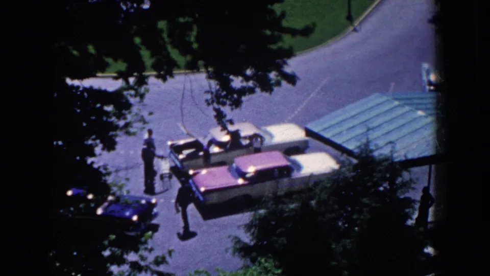 French Lick hotel driveway from above in 1958, showing cars clustered near the green-roofed entrance and pedestrians crossing through shadow.