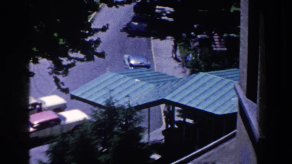 High-angle 1958 French Lick hotel entrance view with a green canopy, partial classic cars, trees, and silhouetted people near the building.